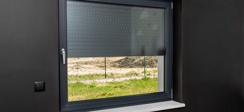 A large window in a room with black walls, half covered with external blinds.
